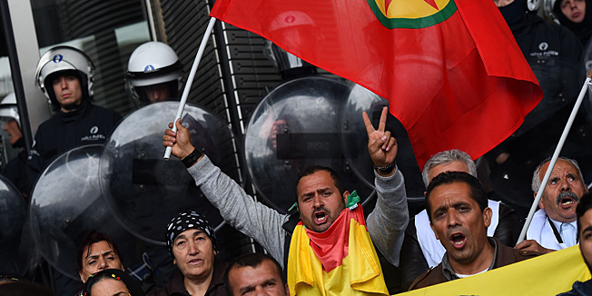Protesters chant slogans while waving a Kurdistan Workers' Party (PKK) flag as riot police guard the main entrance of the European Parliament during a demonstration calling for support for the Syrian Kurdish town of Ain al-Arab, known as Kobane by the Kurds and currently besieged by the Islamic State (IS), in Brussels on October 7, 2014. Islamic State jihadists pushed into the key Syrian town of Ain al-Arab (Kobane) on the Turkish border, seizing three districts in the city's east after fierce street fighting with its Kurdish defenders. AFP PHOTO/EMMANUEL DUNAND
