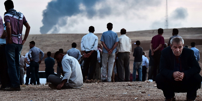 Kurdish people stand on a hill at the Turkish-Syrian border as smoke rises from the Syrian town of Ain al-Arab, known as Kobane by the Kurds, in the southeastern village of Mursitpinar, Sanliurfa province, on October 9, 2014. Advancing Islamic State fighters seized control of a third of the Syrian border town of Kobane Thursday, as Turkey rejected sending in troops on its own against the jihadists. AFP PHOTO / ARIS MESSINIS