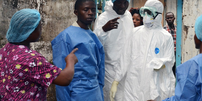 Health workers in protective gear pose at the entrance of the Ebola treatment unit of the John F. Kennedy Medical Center, in the Liberian capital Monrovia, on October 13, 2014. Health workers across Liberia went on strike on Monday to demand danger money to care for the sick at the heart of a raging Ebola epidemic that has already killed dozens of their colleagues. Doctors, nurses and carers in west Africa are on the frontline of the worst-ever outbreak of Ebola, which has killed more than 4,000 people, mostly in Guinea, Sierra Leone and the hardest-hit, Liberia. AFP PHOTO / ZOOM DOSSO