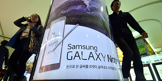 Pedestrians walk past an advert for Samsung Galaxy Note 4 in Seoul on October 30, 2014. Samsung reported a near 50 percent fall in third quarter net profit, as its key smartphone business faltered amid growing competition from Chinese firms in the increasingly saturated market.  AFP PHOTO / JUNG YEON-JE