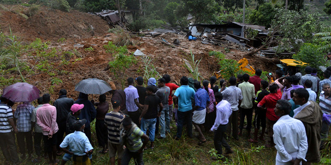 Sri Lankan residents stand near a damaged building at the site of a landslide caused by heavy monsoon rains in Koslanda village in central Sri Lanka on October 29, 2014. Mudslides triggered by monsoon rains swept through a tea-growing region of Sri Lanka October 29, killing at least 16 people and leaving about 300 more feared missing, disaster officials said. AFP PHOTO/ Ishara S. KODIKARA
