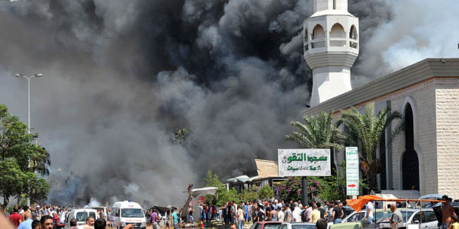 Smoke is seen above people gathering outside a mosque on the site of a powerful explosion in the northern Lebanese city of Tripoli on August 23, 2013. Two powerful explosions killed several people: one rocked the city centre near the home of outgoing Prime Minister Najib Mikati, the second one struck near the port of the restive city with a Sunni Muslim majority. The explosions come a week after a suicide car bombing killed 27 people in a Beirut stronghold of the Lebanese Shiite movement Hezbollah, which is fighting alongside Assad's forces.   AFP PHOTO  IBRAHIM CHALHOUB 