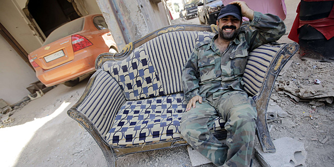 A soldier of the Syrian government forces poses on a sofa on July 31, 2013 in the destroyed district of al-Khalidiyah in the central Syrian city of Homs. The Syrian government announced the capture of Khalidiyah, a key rebel district in Homs, Syria's third city and a symbol of the revolt against President Bashar al-Assad. AFP PHOTO/JOSEPH EID