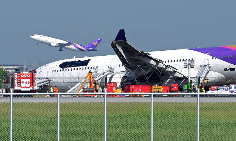 A Thai Airways plane (L) takes off as another (R), with its logo and name covered up, rests on ground the morning after it skidded off the runway at Suvarnabhumi International Airport in Bangkok on September 9, 2013. The incident late on September 8, which injured more than a dozen passengers, involved an Airbus 330-300 carrying 287 passengers and 14 crew members on a flight from Guangzhou, the carrier said.     AFP PHOTO / PORNCHAI KITTIWONGSAKUL