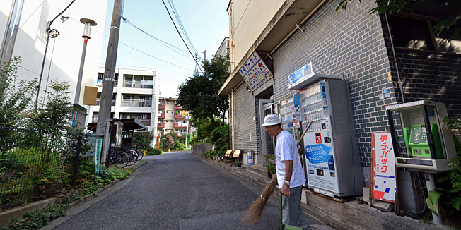 To go with Japan-Oly-2020-JPN,FOCUS by Shigemi SATO In this picture taken on September 14, 2013, 79-year-old resident Kohei Jinno sweeps and cleans a road before his apartment complex near the rebuilt national stadium in Tokyo.  Tokyo's successful bid to host the Olympics made much of plans to re-use venues built for Japan's last Summer Games. But for Kohei Jinno, redevelopment for 2020 means eviction again, just like for 1964. In 1964, his home and business were torn down to make way for an Olympic park around the main stadium for the Tokyo Games. Now he has been told he must move again to make way for the stadium's redevelopment and expansion in time for 2020. AFP PHOTO / Yoshikazu TSUNO