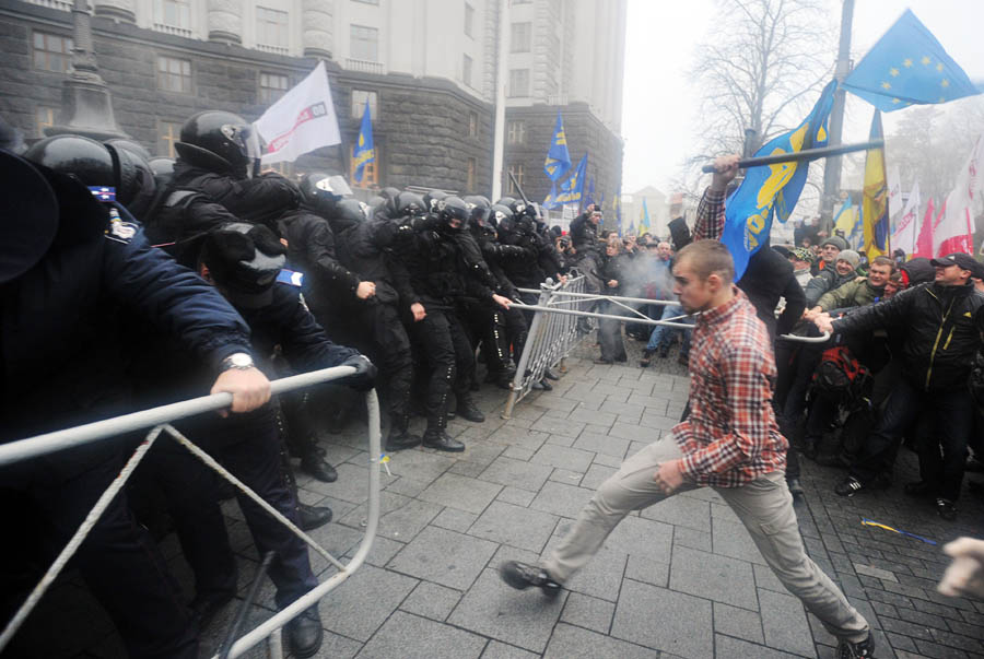 Protesters and riot police clash in front of the Cabinet of Ministers of Ukraine during a rally in Kiev on November 24, 2013. Thousands of pro-Europe protesters in Ukraine attempted to storm the government building in the capital of Kiev Sunday, clashing with police who fired tear gas to keep them back. Protesters tried to break through police ranks surrounding the building, with some throwing stones and hitting officers with the signs they were carrying, as police fought back with batons, an AFP correspondent reported. AFP PHOTO / GENYA SAVILOV