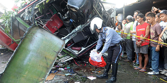 A highway patrol officer collects belonging of passengers of the bus that fell from an elevated highway in Manila on December 16, 2013. Twenty-two people were killed when a commuter bus plunged from an elevated highway onto a van in Philippine capital, police said, warning the death toll could rise. AFP PHOTO / Jay DIRECTO