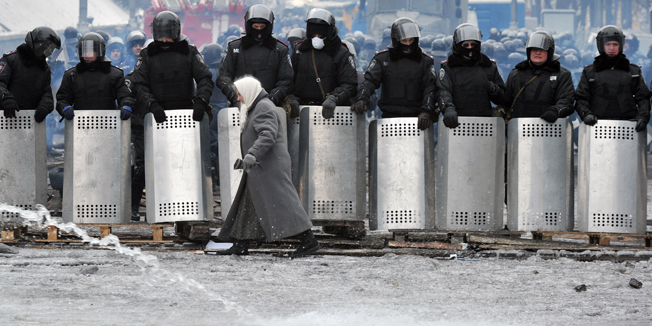 A woman walks in front of riot police troops on Grushevsky Street near European square in central Kiev on January 28, 2014. Ukrainian lawmakers scrapped on January 28 draconian anti-protest laws that have angered the opposition, in a move aimed at bringing a deadly two-month standoff to an end. AFP PHOTO / GENYA SAVILOV