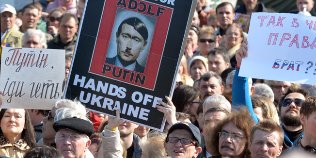 People hold placard portraying Russian President Vladimir Putin as Adolf Hitler and reading 
