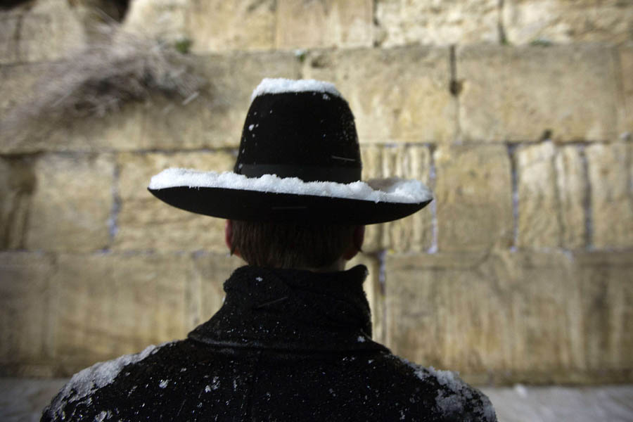 A Jewish man prays at the Western Wall as snow falls in the old city of Jerusalem on January 10, 2013. Jerusalem was transformed into a winter wonderland after heavy overnight snowfall turned the Holy City and much of the region white, bringing hordes of excited children onto the streets. AFP PHOTO/MENAHEM KAHANA