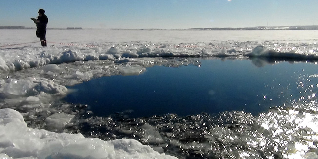 A handout photo taken on February 15, 2013, and provided by Chelyabinsk region police department shows a police officer standing near a six-metre (20-foot) hole in the ice of a frozen lake, reportedly the site of a meteor fall, outside the town of Chebakul in the Chelyabinsk region. Divers scoured today  the bottom of a Russian lake for fragments of a meteorite that plunged to Earth in a blinding fireball whose shockwave injured 1,200 people and damaged thousands of homes. AFP PHOTO / CHELYABINSK REGION POLICE DEPARTMENT-- RESTRICTED TO EDITORIAL USE - MANDATORY CREDIT 