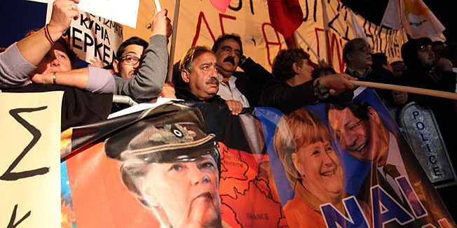Cypriot protestors wave banners picturing German Chancellor Angela Merkel (C) and Cypriot President Nicos Anastasiades (R) during a demonstration against an EU bailout deal outside the parliament in the capital, Nicosia, on March 19, 2013. The speaker of the Cypriot parliament urged MPs to say 