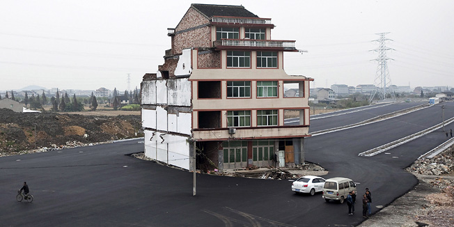 FILE - In this Nov. 22, 2012 file photo, people stand near a house sitting in the middle of a new main road on the outskirts of Wenling city in east China's Zhejiang province. Duck farmer Luo Baogen and his wife are the lone holdouts from a neighborhood of once-connected homes that was demolished to make way for the main thoroughfare heading to a newly built railway station. (AP Photo/File) CHINA OUT