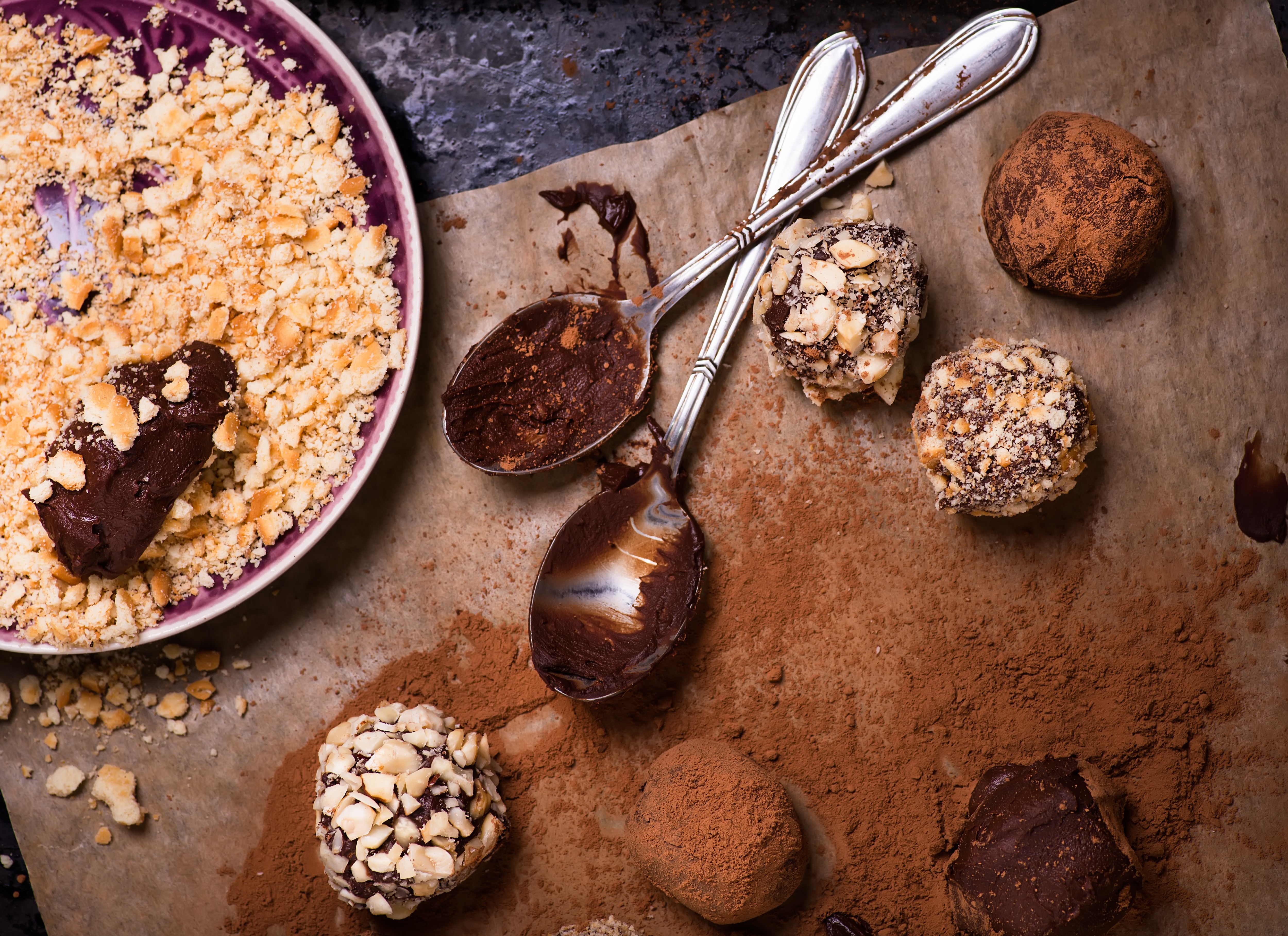 Assorted dark chocolate truffles with cocoa powder, biscuit and chopped hazelnuts over baking paper, selective focus