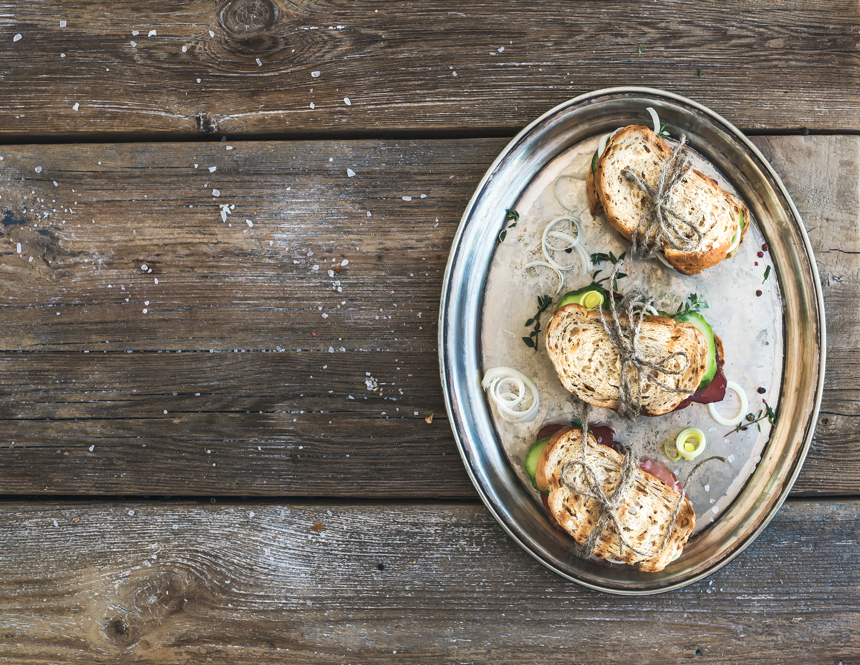 Rustic sandwich set. Sandwiches with smoked meat, cucumber, onion, herbs and spices on metal dish over rough wood background, copy space