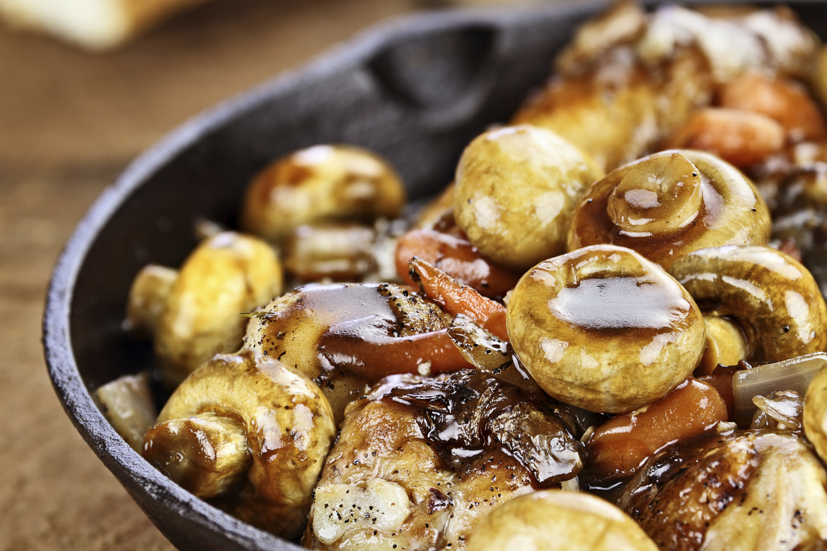 Detailed shot of Coq Au Vin in rustic cast iron pan with shallow depth of field.