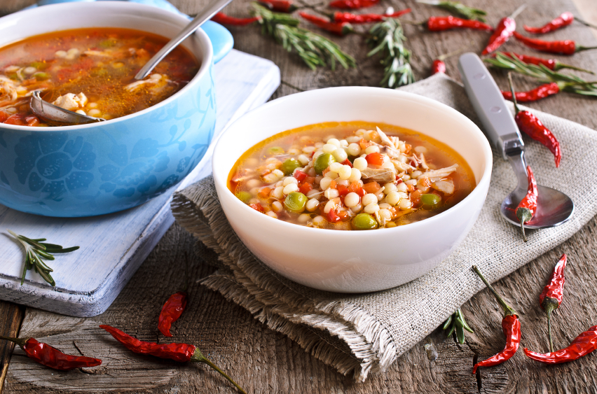 Soup with small pasta, vegetables and pieces of meat in a ceramic bowl on a wooden surface