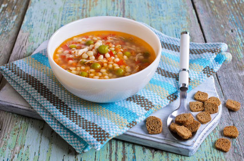 Soup with small pasta, vegetables and pieces of meat in a ceramic bowl on a wooden surface
