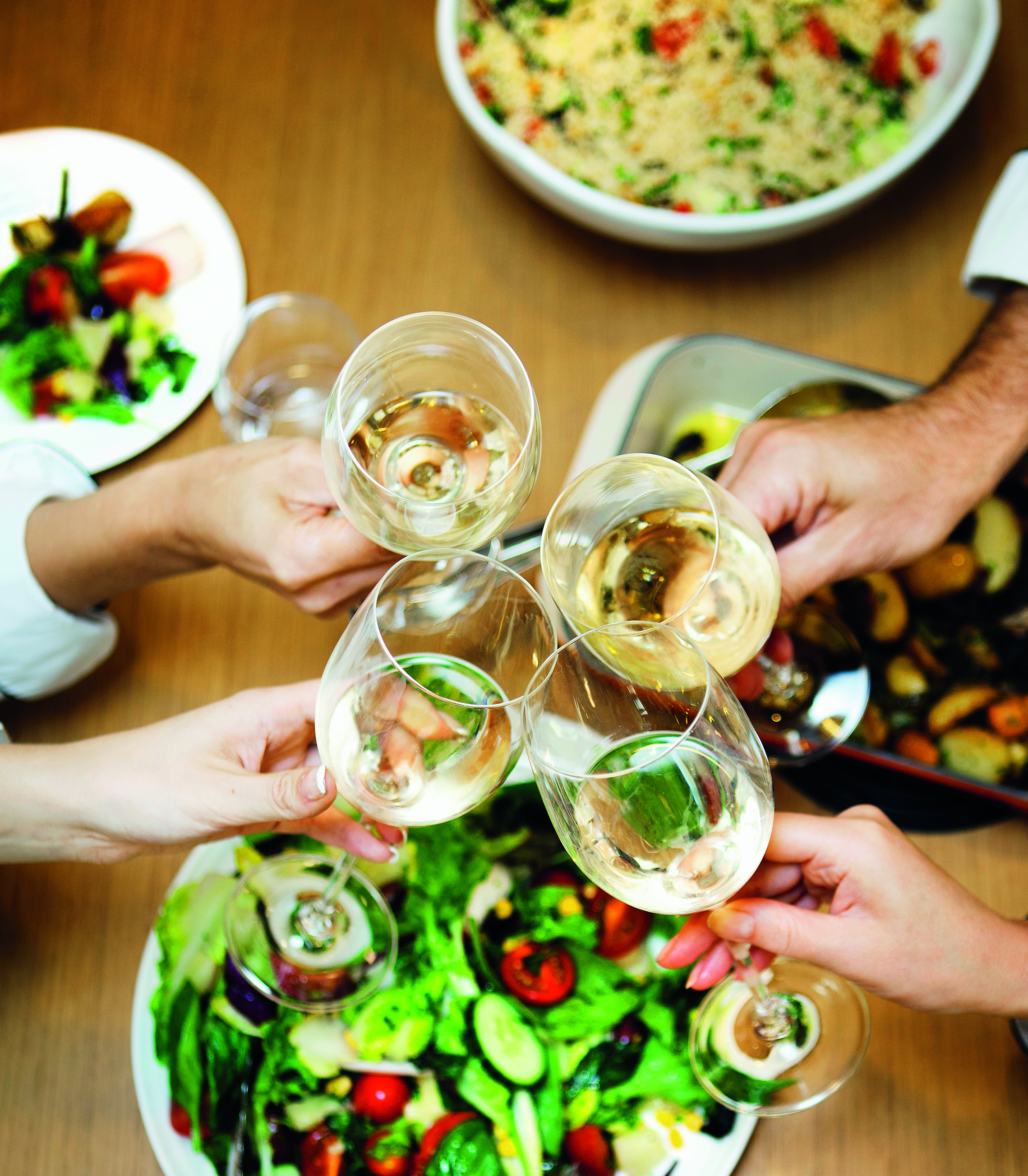 Four people sitting at a laid table toasting with wine glasses