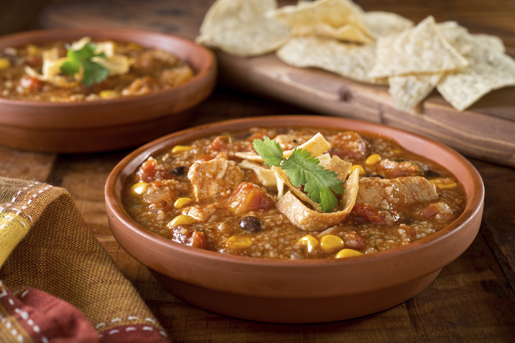 A bowl of delicious home made chicken tortilla soup with chicken, corn, black bean, tomato, homini, and tortilla.