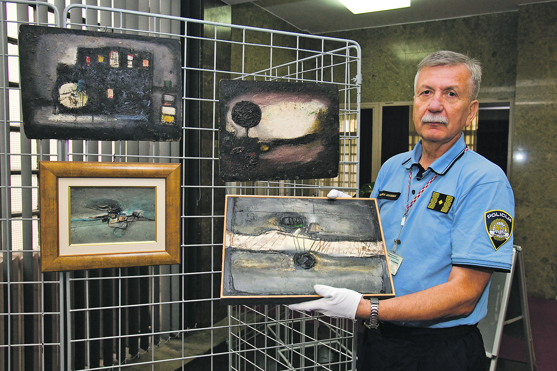 Željko Jamičić, voditelj Muzeja policije, u rukama drži originalni rad Ljube Ivančića, dok su na paravanu obješeni falsifikati