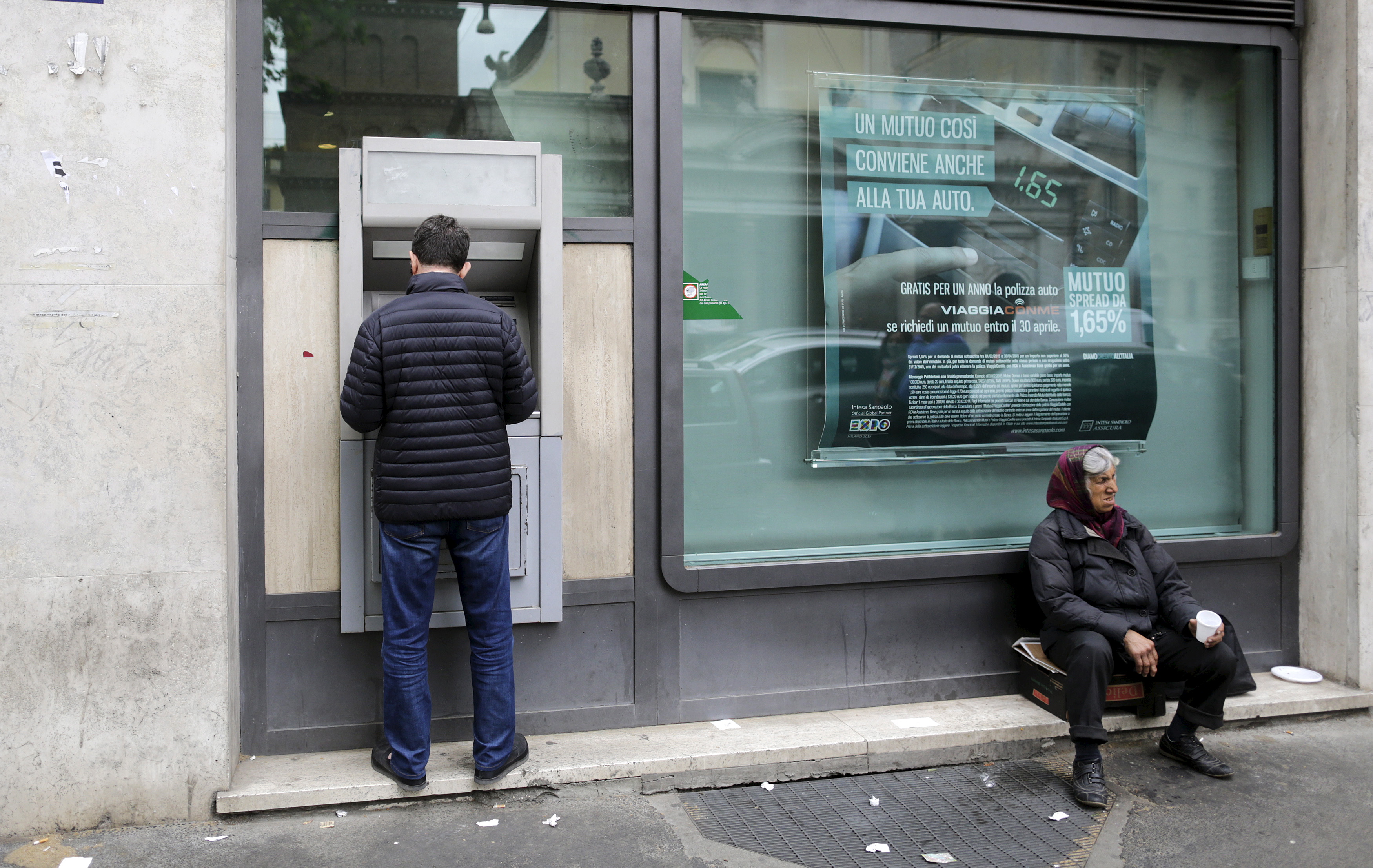 Muškarac podiže novac na bankomatu dok nedaleko od njega žena prosi