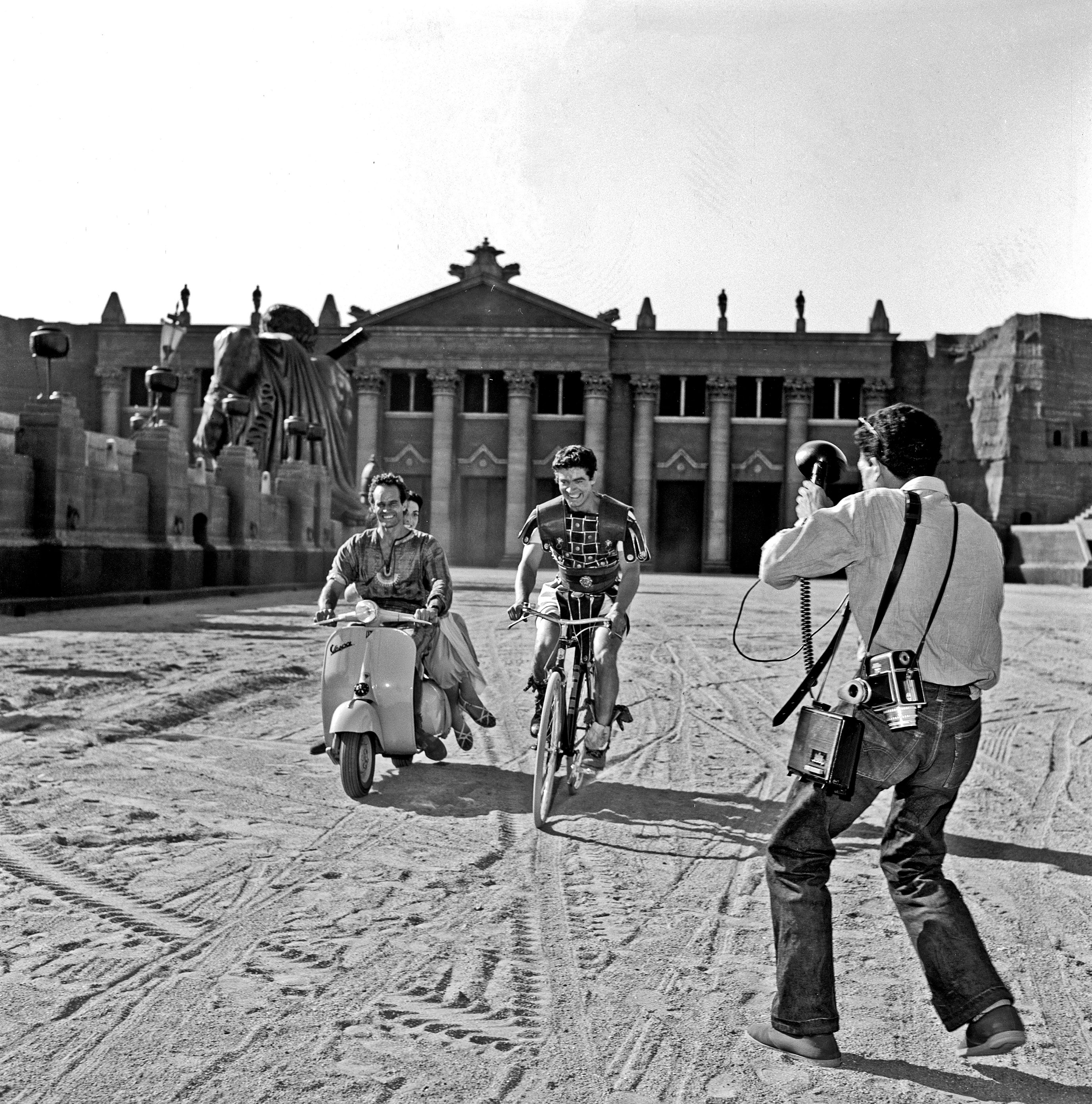 Charlton Heston i Stephen Boyd na setu filma “Ben Hur” Williama Wylera u starorimskim kostimima voze se na Vespi i biciklu u studijima Cinecittà, 1958.