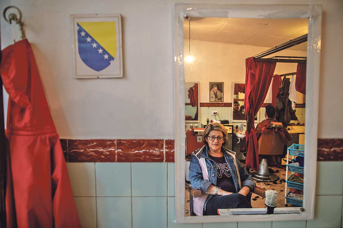 U centru Bihaća, iza crvenog zastora skoro uvijek navučenog preko izloga, dvanaest vrlo urednih Pakistanaca nabilo se u malu prostoriju od petnaestak kvadrata. Na stolici u kutu sjedi, puši i sluša ih Orana, njihova Mama. Orana je vlasnica malog frizerskog salona, jednog od rijetkih mjesta gdje su migranti dobrodošli i kada nemaju novca ni nekog posebnog posla.
“Meni je njih žao. Kad ih počnu kupiti, ko životinje da kupe. Fuj”, priča. Iako dosta sugrađana zbog toga negoduje, a neki je po društvenim mrežama i vrlo uvredljivo prozivaju, Oranina vrata su migrantima otvorena otkad je kriza u Bihaću počela. I ona ih ne misli zatvarati, bez obzira na pritiske i kazne kojima joj prijete.
Drugi joj se dive. Profesor, stara mušterija još otkad je salon držao Oranin otac, “prijeti” joj da više nikada neće doći ako prestane pomagati migrantima.
Hrabra žena je jedan od heroja ove teške priče, i čovjek prije svega. Jedna od rijetkih volontera koje sam u Bihaću sreo, a nije ih malo, koju nije strah da joj se ime i slika pojavi u novinama. Čega je ostale strah? Nas samih?