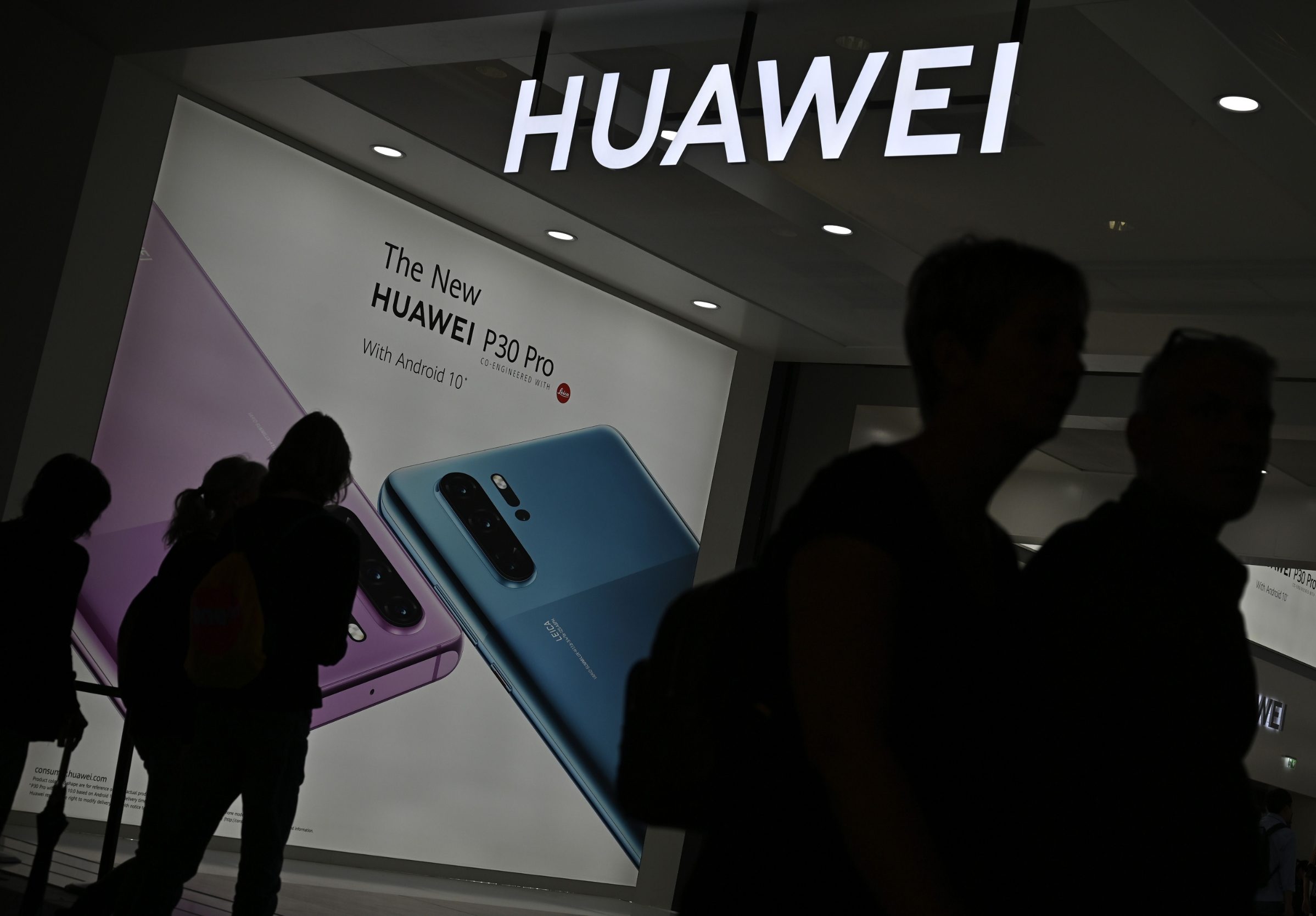 Ilustracija: prolaznici ispred promotivnog plakata tvrtke Huawei