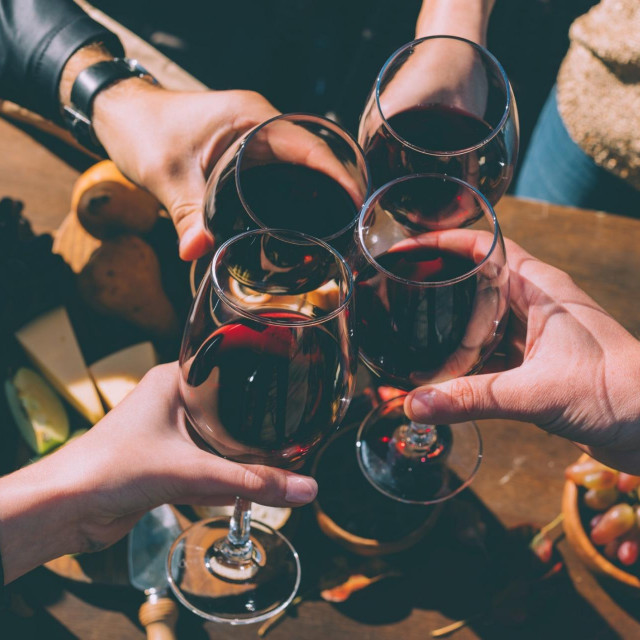cropped shot of group of people clinking glasses of delicious red wine