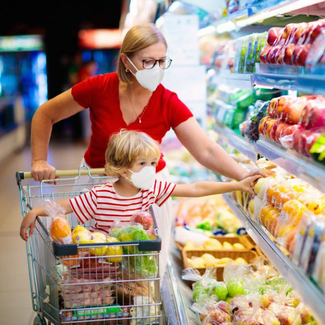 Shopping with kids during virus outbreak. Mother and child wearing surgical face mask buying fruit in supermarket. Mom and little boy buy fresh vegetable in grocery store. Family in shop.