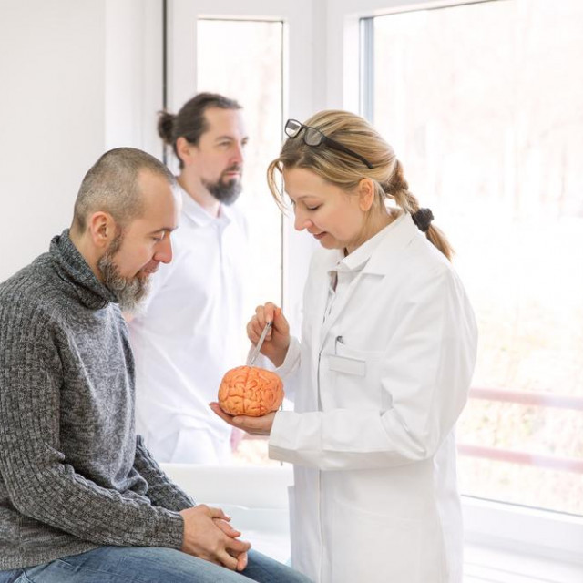 female neurologist is showing a male patient something on a synthetic brain