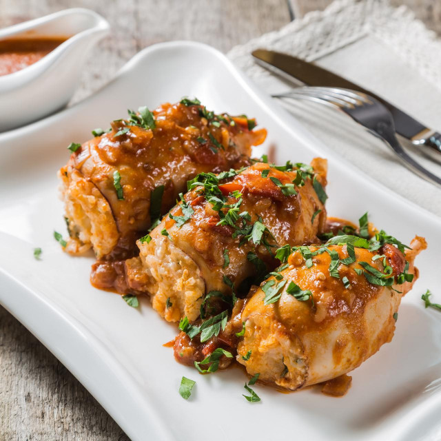 Squid stuffed with rice, olives and feta cheese in tomato sauce on a table of old boards