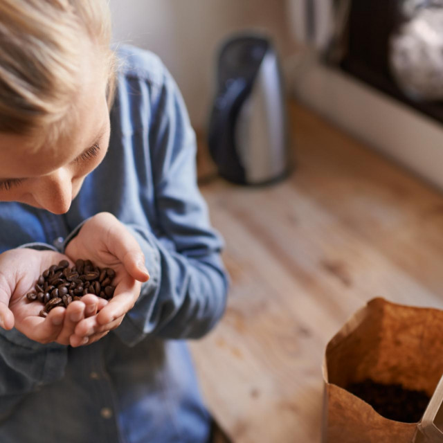 A young woman smelling fresh coffee beans in her kitchen