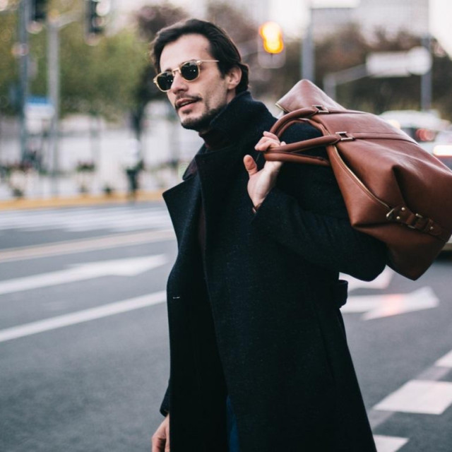 Handsome modern man on a lovely day out in the city. He is holding a bag.