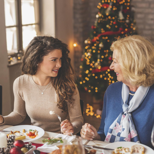 Family having Christmas dinner at home, gathered around the table, enjoying their time together; daughter speaking to her mother and smiling