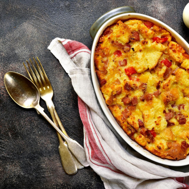 Bread pudding with bacon and cheese in a baking dish over dark slate,stone or metal background.Top view.