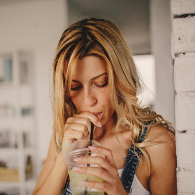 Photo of a young smiling woman having healthy smoothie for a snack meal