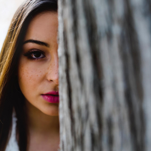Teenage girl half face behind the trunk in the park nature