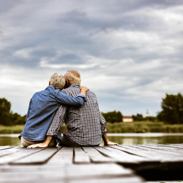 Back view of embraced mature couple looking at view while relaxing on a jetty at river. Copy space.