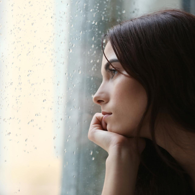 Depressed young woman near window at home, closeup