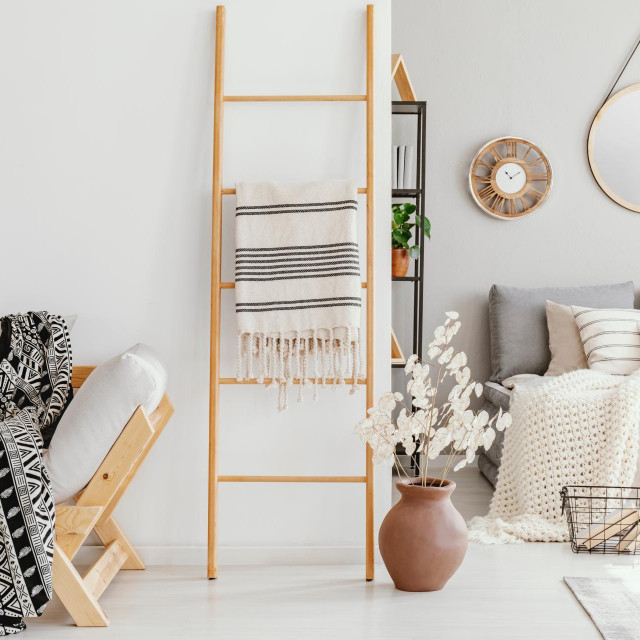 Wooden ladder with blanket between elegant settee with patterned blanket and comfortable bed with light grey bedding, real photo