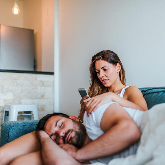 Jelous young woman cheking boyfriend's phone while he sleeps.