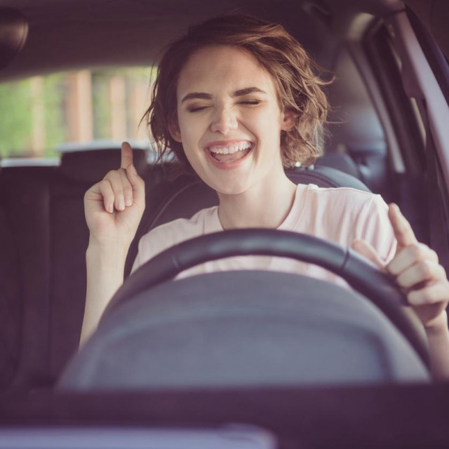 Photo of positive cheerful girl ride drive car town route wait traffic jam listen, music sound try dance feel excited