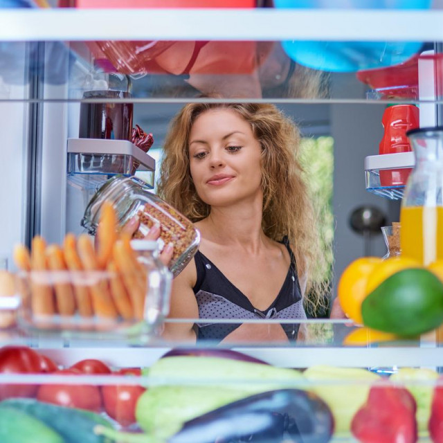 Woman taking food from fridge full of groceries. Picture taken from the inside of fridge.