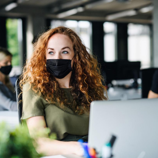Thoughtful young woman with face mask back at work in office after lockdown.