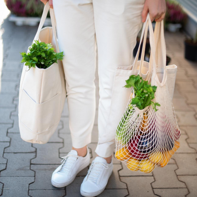 Girl is holding mesh shopping bag and cotton shopper with vegetables without plastic bags at farmers market. Zero waste, plastic free concept. Sustainable lifestyle. Banner