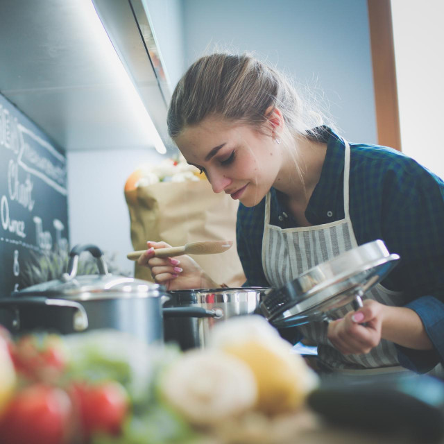 Young woman cooking in her kitchen standing near stove