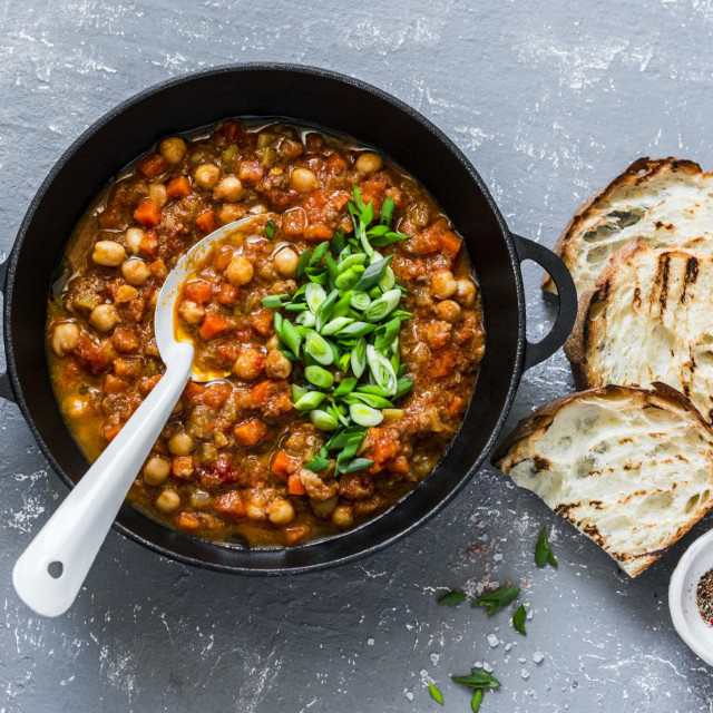 Vegetarian mushrooms chickpea stew in a iron pan and rustic grilled bread on a gray background, top view. Healthy vegetarian food concept. Vegetarian chili
