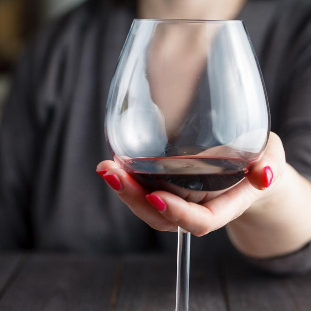 woman drinking alcohol on dark background. Focus on wine glass
